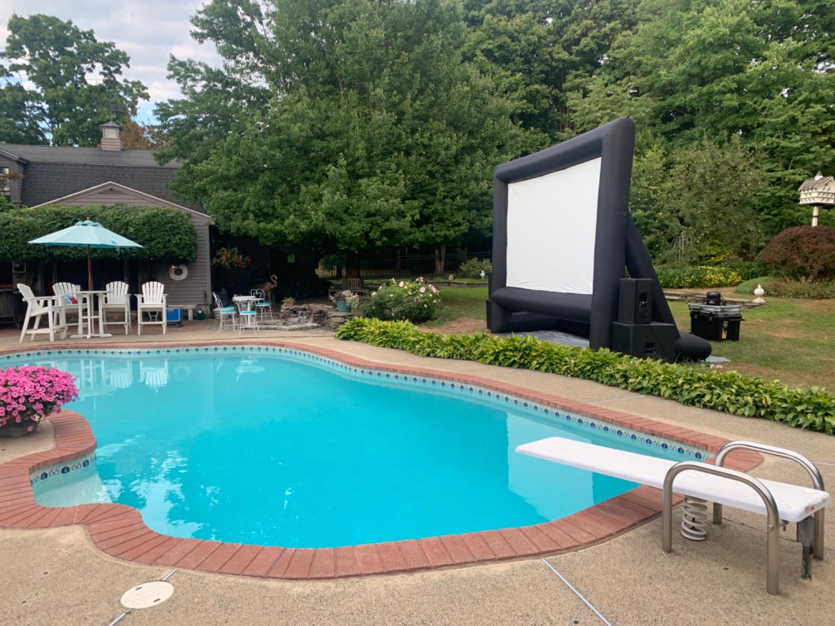 Large inflatable movie screen set up next to a pool with lush garden