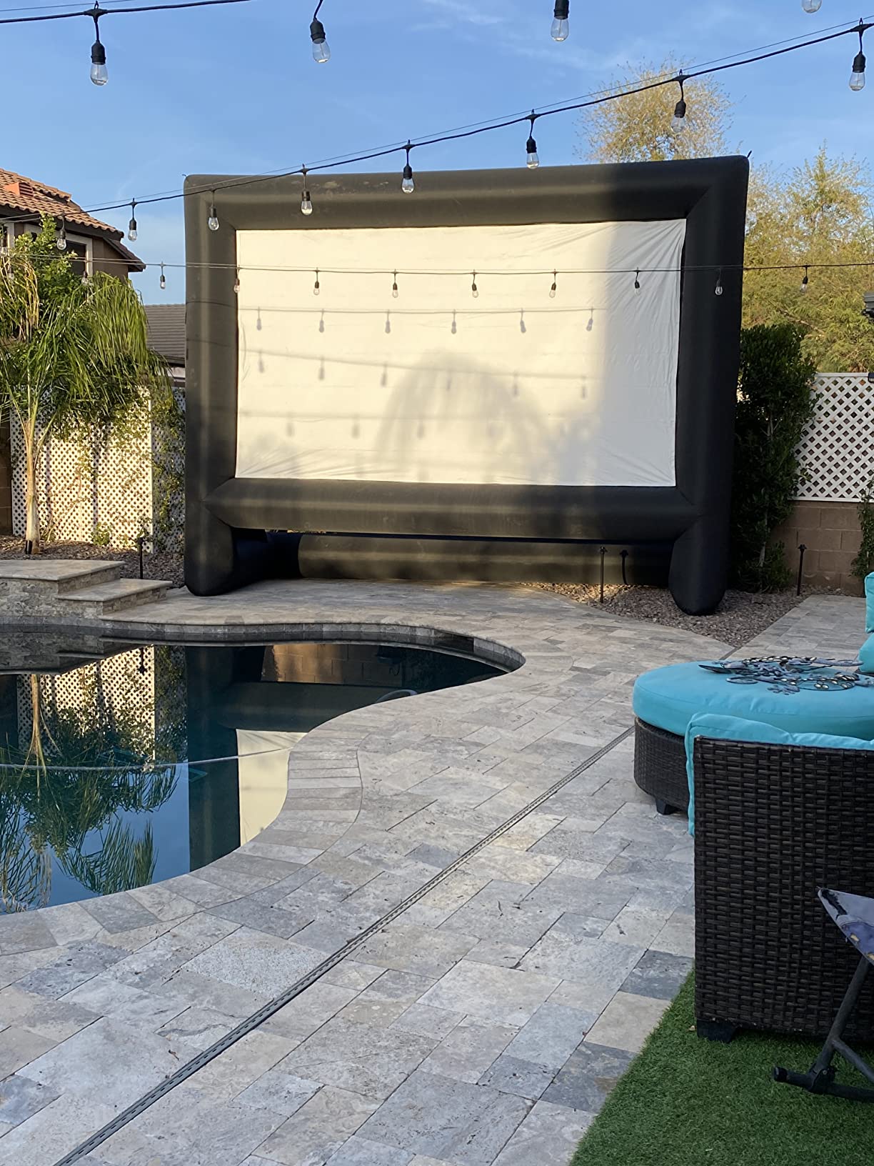 Outdoor movie screen beside a pool with string lights at dusk